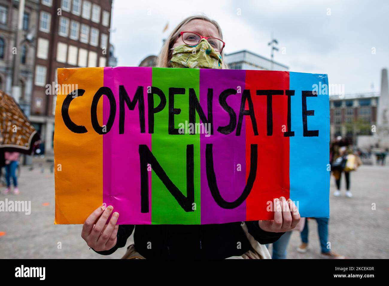a-woman-is-holding-a-placard-that-says-compensation-now-during-the