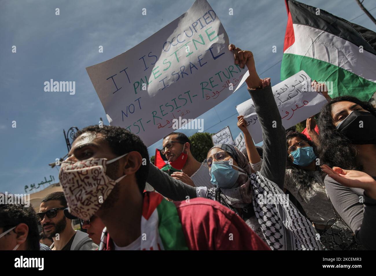 A female protester lifts a placard that reads in english, it is called Occupied Palestine not Israel, Resist, Return, as other protesters wave the Palestinian flag during a demonstration held by thousands of Tunisian an Palestinian demonstrators on avenue Habib Bourguiba in the capital Tunis, Tunisia, on May 15, 2021, in support with the Palestinian people and to protest against the Israel's air strikes on Gaza strip and against the Israeli violations in the occupied territories in Palestine, especially in the Palestinian neighborhood in East Jerusalem, Sheikh Jarrah. (Photo by Chedly Ben Ibra Stock Photo