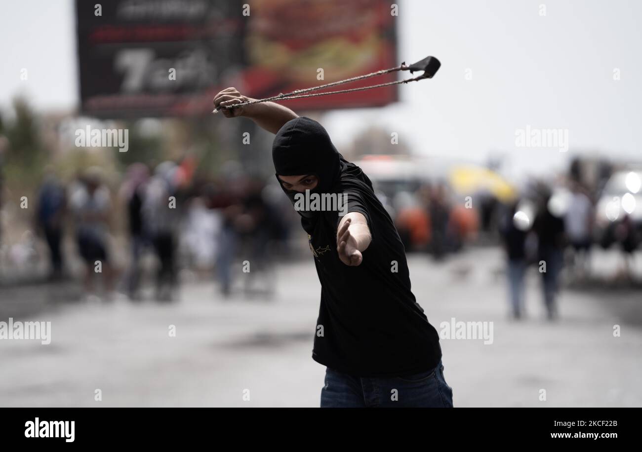 A Palestinian demonstrator uses a slingshot next to burning tires