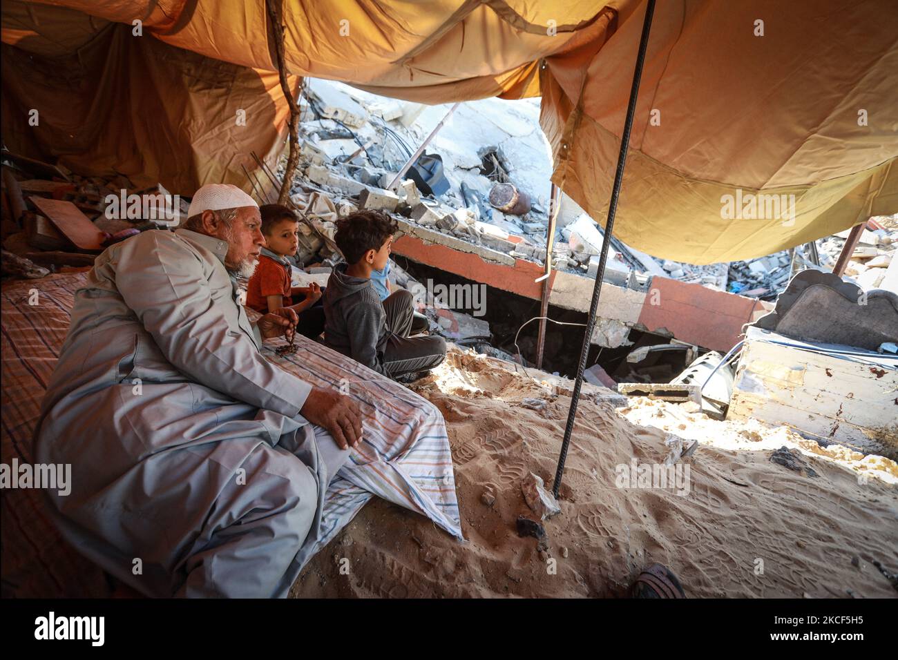 Palestinians sit in a makeshift tent amid the rubble of their houses ...