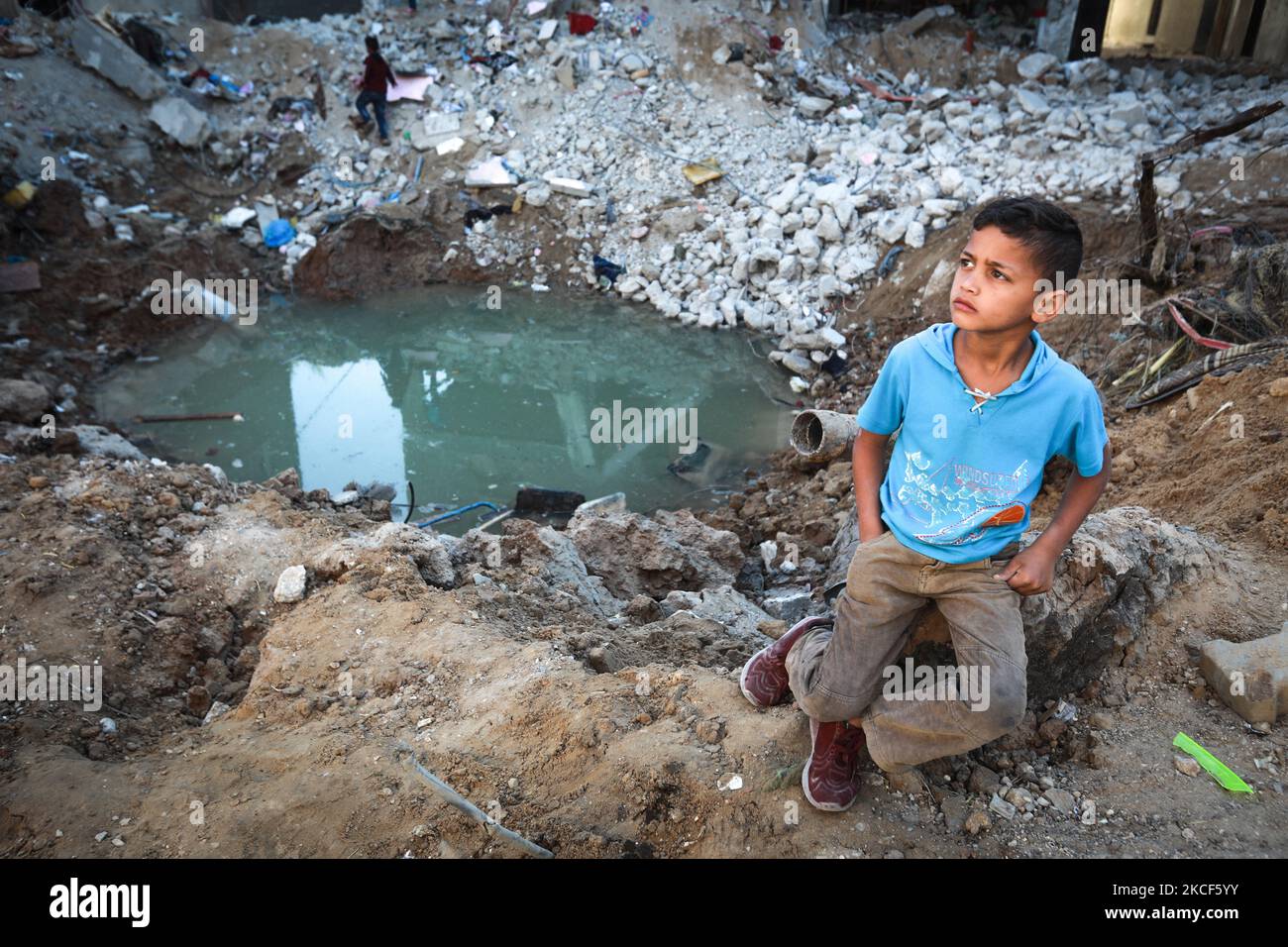 Palestinian children walk through the rubble next to a crater on May 24 ...