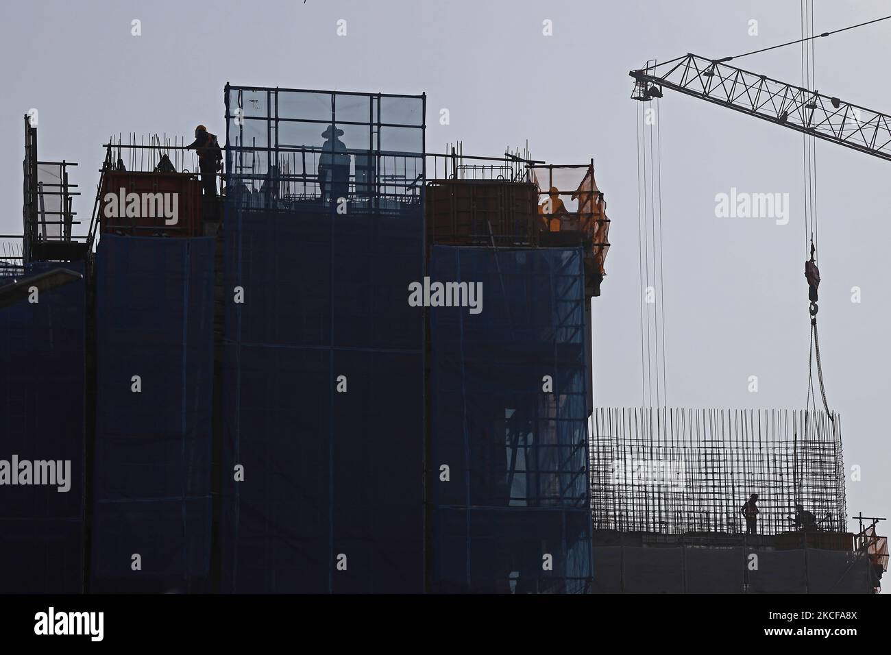 Migrant workers work at a building construction site on May 28, 2021 in Singapore. Singapore enters a month long heightened alert from May 16 to June 13 to curb the spread of COVID-19 cases in the local community. New restrictions on movements and activities have been introduced such as limiting social interaction to two, prohibiting dining out and a reduced operating capacity at shopping malls, offices and attractions. On May 17, the construction industry stakeholders appealed to Multi-Ministry Taskforce to bring in foreign workers in a safe and controlled manner after the built environment i Stock Photo