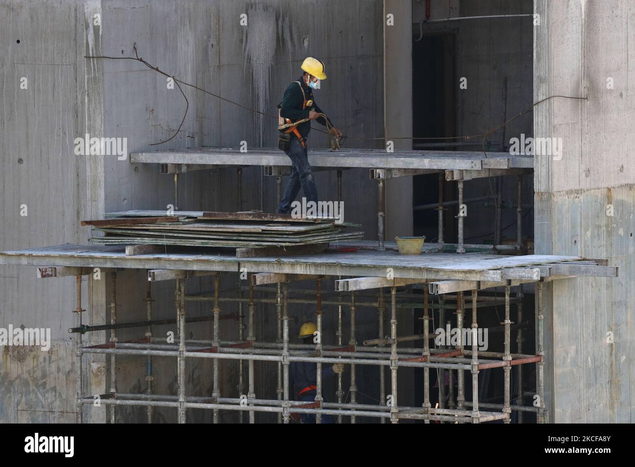 Migrant workers work at a building construction site on May 28, 2021 in Singapore. Singapore enters a month long heightened alert from May 16 to June 13 to curb the spread of COVID-19 cases in the local community. New restrictions on movements and activities have been introduced such as limiting social interaction to two, prohibiting dining out and a reduced operating capacity at shopping malls, offices and attractions. On May 17, the construction industry stakeholders appealed to Multi-Ministry Taskforce to bring in foreign workers in a safe and controlled manner after the built environment i Stock Photo