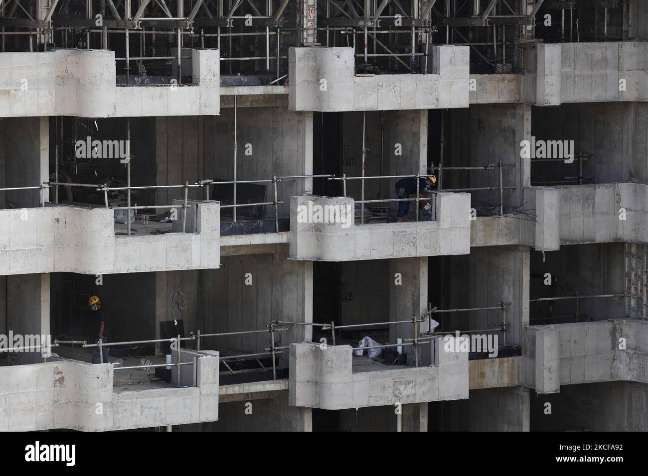 Migrant workers work at a building construction site on May 28, 2021 in Singapore. Singapore enters a month long heightened alert from May 16 to June 13 to curb the spread of COVID-19 cases in the local community. New restrictions on movements and activities have been introduced such as limiting social interaction to two, prohibiting dining out and a reduced operating capacity at shopping malls, offices and attractions. On May 17, the construction industry stakeholders appealed to Multi-Ministry Taskforce to bring in foreign workers in a safe and controlled manner after the built environment i Stock Photo