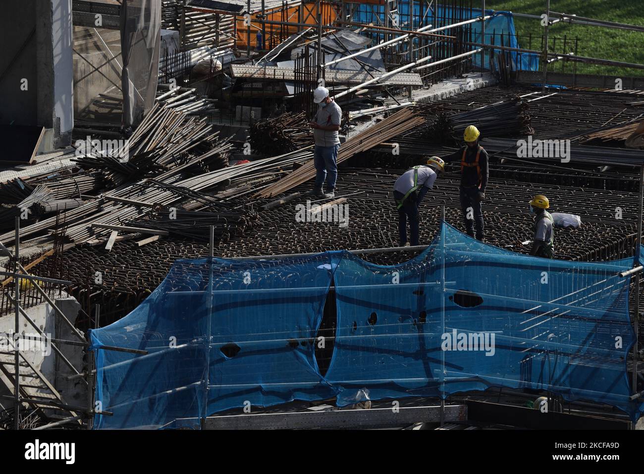 Migrant workers work at a building construction site on May 28, 2021 in Singapore. Singapore enters a month long heightened alert from May 16 to June 13 to curb the spread of COVID-19 cases in the local community. New restrictions on movements and activities have been introduced such as limiting social interaction to two, prohibiting dining out and a reduced operating capacity at shopping malls, offices and attractions. On May 17, the construction industry stakeholders appealed to Multi-Ministry Taskforce to bring in foreign workers in a safe and controlled manner after the built environment i Stock Photo