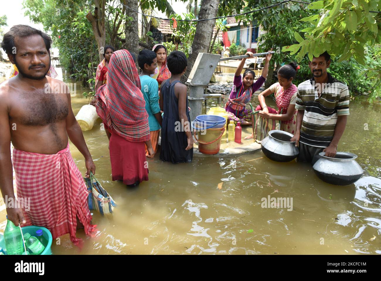 Villagers gathered to collect drinking water from the only left tube well. All other handpumps are completely under water right now. On May 28, 2021 in West Bengal, India. According to report more than three hundred thousand homes were destroyed and the people directly were affected by the severe cyclone Yaas, as sea waters along the Bengal coast and rivers started swelling and breached embankments, after the landfall at Odisha at 9.30am on 26 May 2021. Various farms were directly affected by the salt water reached in the farming areas. The cities narrowly escaped from the cyclone hit but rema Stock Photo