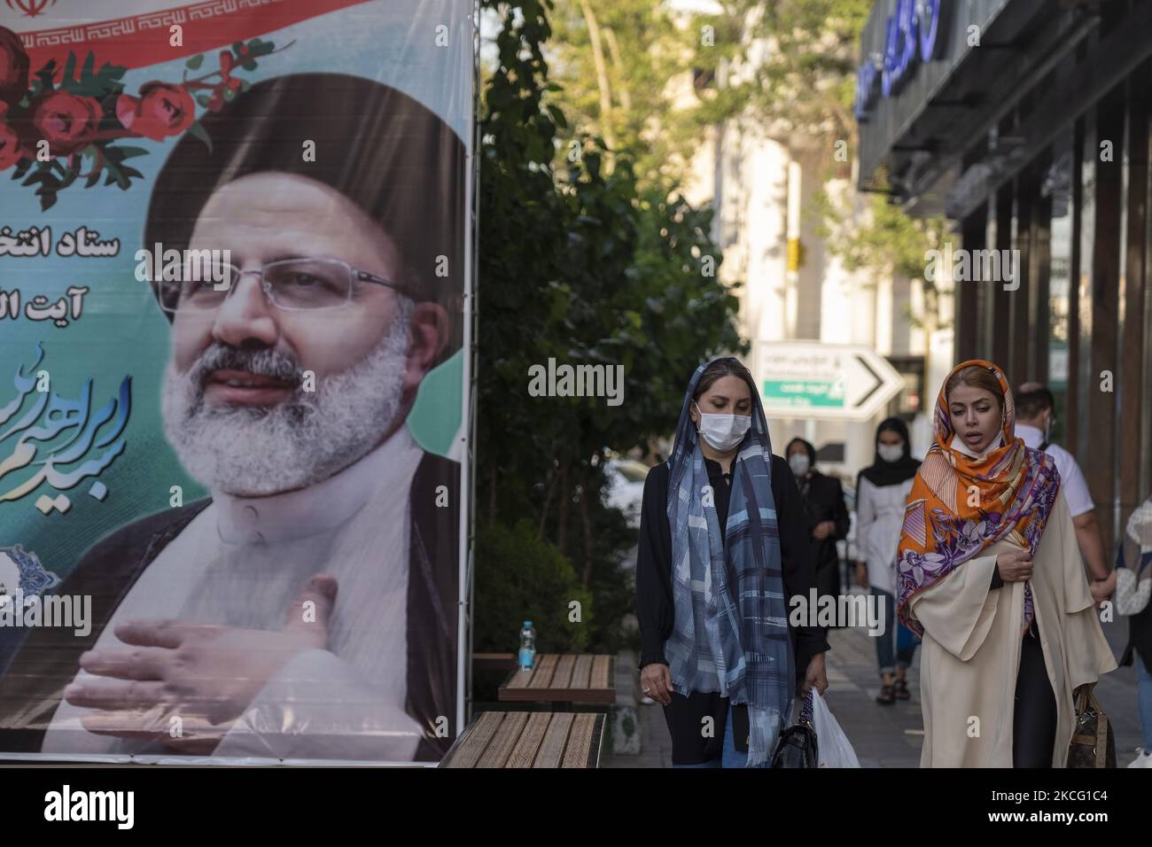 Two Iranian women walk past a presidential elections candidate Ebrahim Raisi’s electoral banner which is hanged on a street-side out of a Raisi’s campaign center in northern Tehran during the days of Iran’s presidential elections campaigns on June 12, 2021. (Photo by Morteza Nikoubazl/NurPhoto) Stock Photo