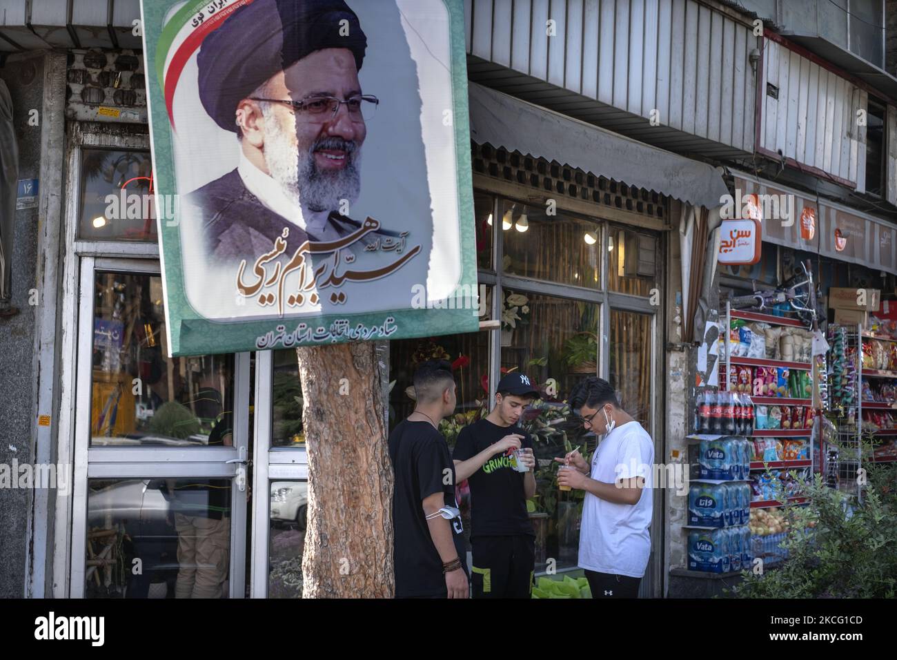 Iranian youth eat ice creams while standing under a presidential elections candidate Ebrahim Raisi’s banner which is hanged from a tree on a street-side in downtown Tehran during the days of Iran’s presidential elections campaigns on June 12, 2021. (Photo by Morteza Nikoubazl/NurPhoto) Stock Photo