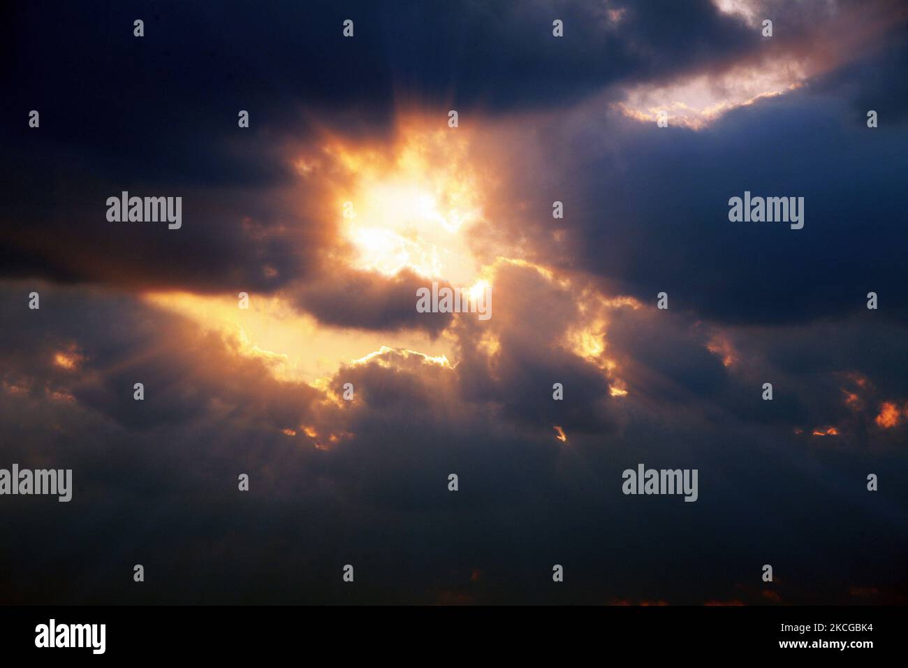 Sun rays and red rays shining through the dark clouds in the cloudy sky Stock Photo