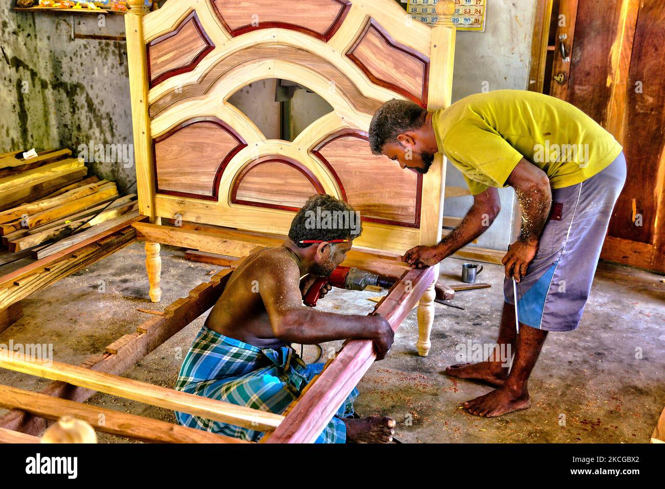 Carpenters construct a fancy wooden bed frame at a small workshop in ...