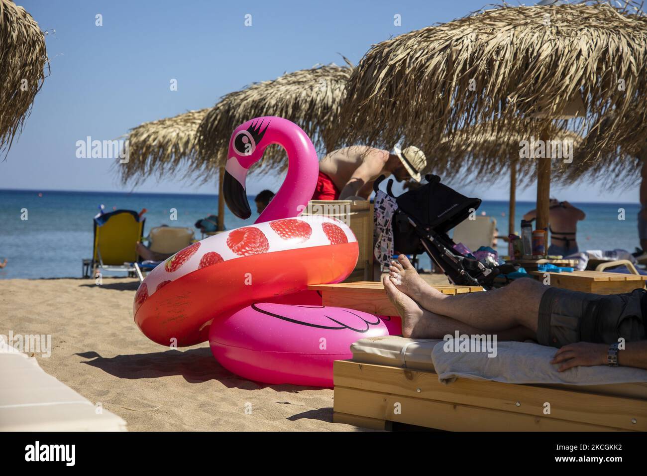 Sea Inflatables Rhodes A tourist rests under the beach umbrella by a pink inflatable flamingo ...