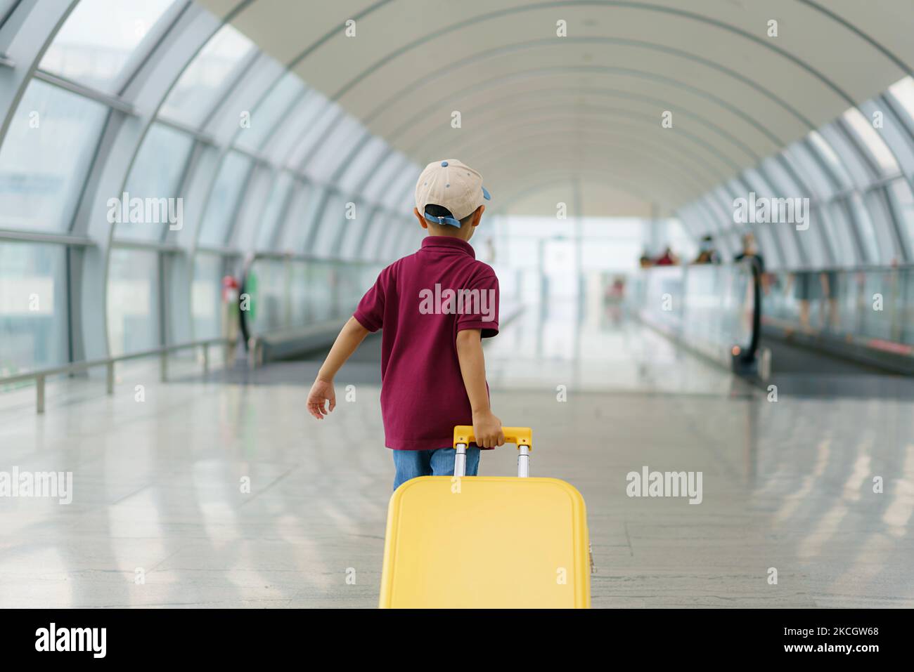 Asian boy with yellow suitcase wear T-shirt and shorts walking in airport terminal prepare to boarding at gate for plane flight. Stock Photo