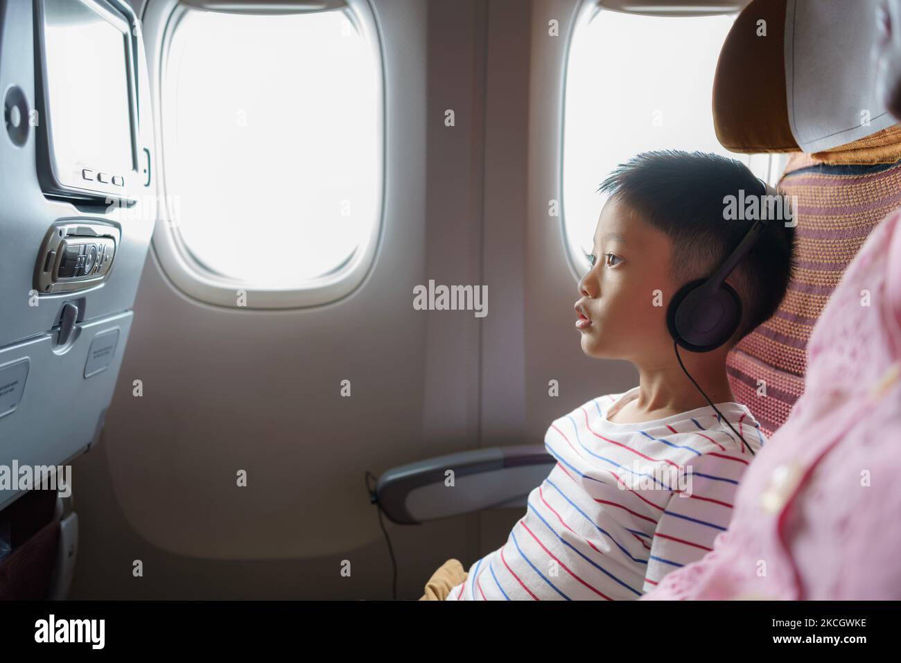 Asian kid enjoying and watching cartoons with his mother during the long flight in airplane. Child travel journey vacation concept. Stock Photo
