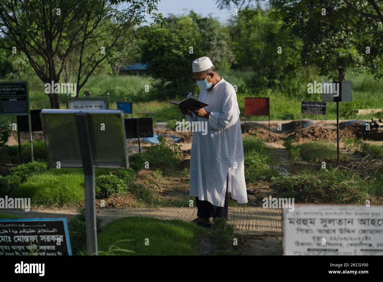 A man is reciting the Holy Quran in front of his son's grave who died due to covid 19 in Dhaka, Bangladesh, on July 5, 2021. As the number of covid patients increases, Bangladesh declared strict lockdown nationwide. (Photo by Istiak Karim/NurPhoto) Stock Photo