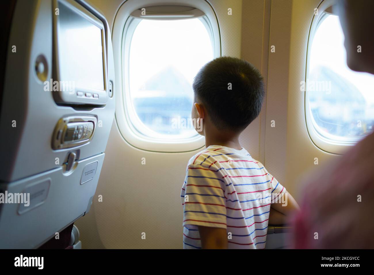Asian children look at the aerial view of the sky and clouds outside the plane window while sitting on the plane seat. Stock Photo