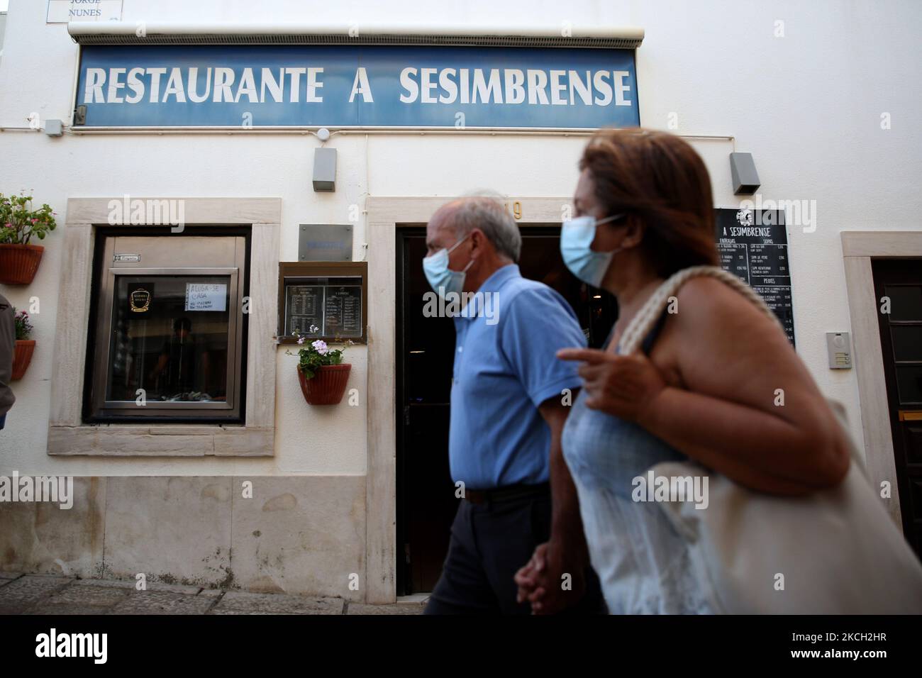 People wearing face masks walk by a restaurant in Sesimbra, outskirts