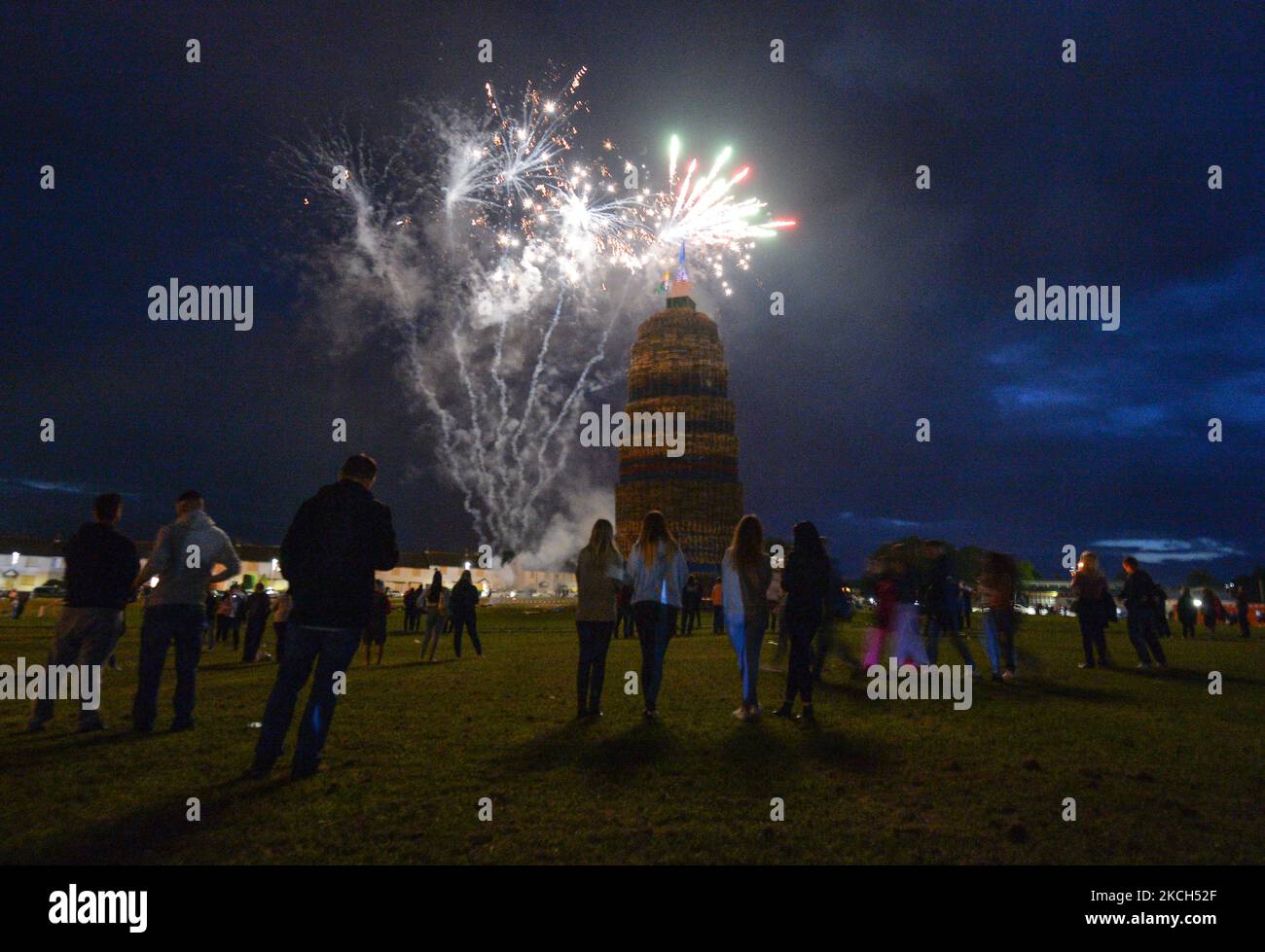 People watch fireworks as they wait for a large bonfire to be lit during the Eleventh Night celebration organized by members of the Loyalist Order in Craigy Hill, Larne. Tonight, large bonfires are lit in many Protestant loyalist neighbourhoods of Northern Ireland. Bonfires were originally lit to celebrate the Glorious Revolution (1688) and victory of Protestant king William of Orange over Catholic king James II at the Battle of the Boyne (1690), which began the Protestant Ascendancy in Ireland. On Monday, 12 July 2021, in Larne, County Antrim, Northern Ireland (Photo by Artur Widak/NurPhoto) Stock Photo