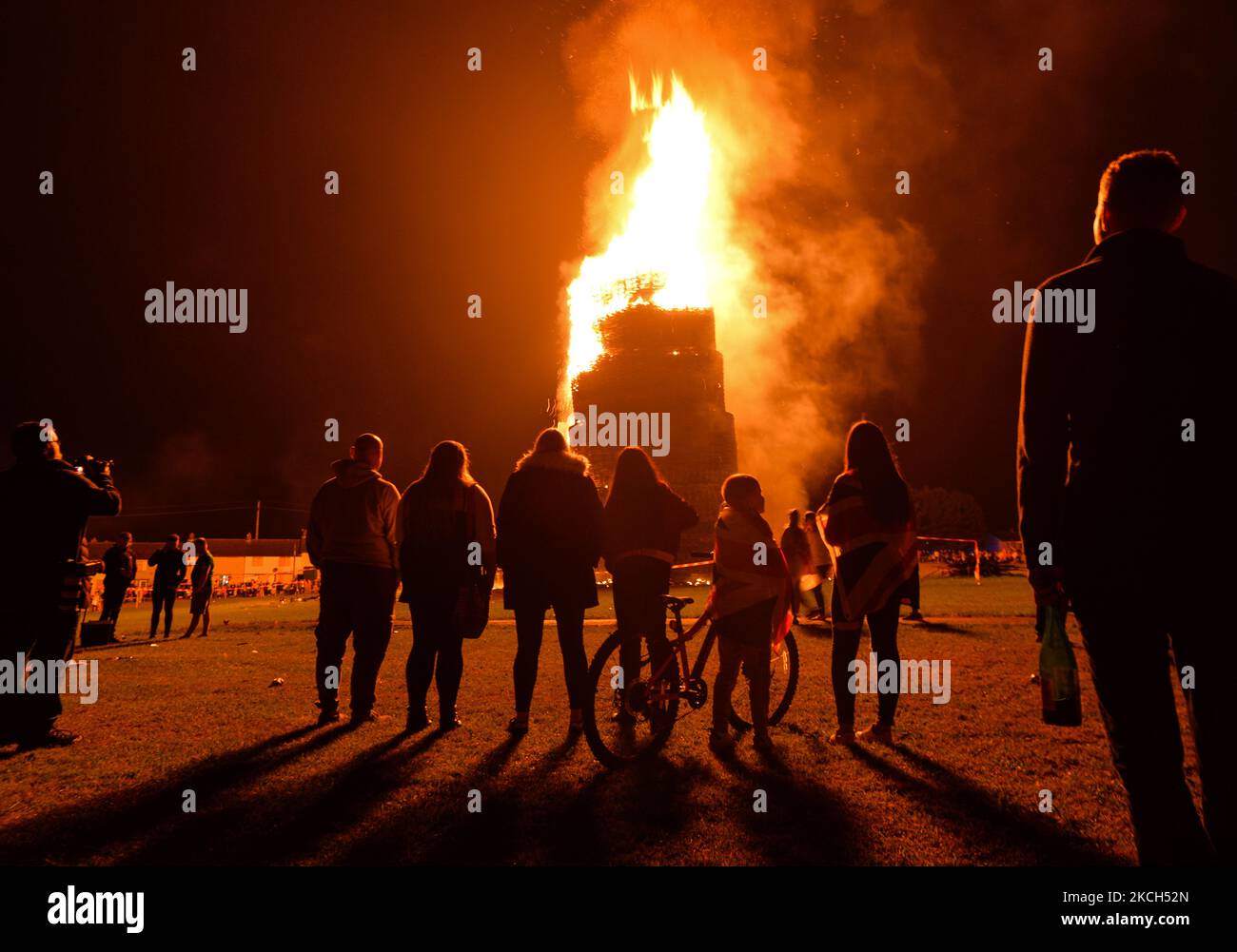 People watch a large bonfire during the Eleventh Night marking the start of the unionist Twelfth celebrations, in Craigy Hill, Larne. Tonight, large bonfires are lit in many Protestant loyalist neighbourhoods of Northern Ireland. Bonfires were originally lit to celebrate the Glorious Revolution (1688) and victory of Protestant king William of Orange over Catholic king James II at the Battle of the Boyne (1690), which began the Protestant Ascendancy in Ireland. On Monday, 12 July 2021, in Larne, County Antrim, Northern Ireland (Photo by Artur Widak/NurPhoto) Stock Photo