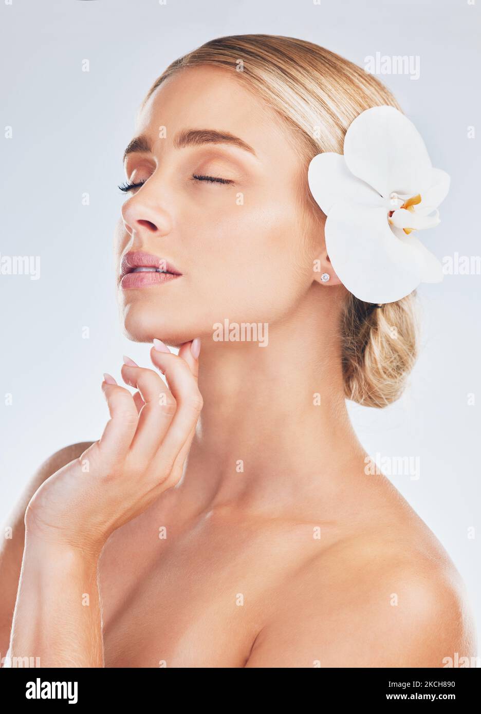 Skincare, wellness and face of a woman with an orchid for health, beauty and dermatology against a grey studio background. Spa, flower and girl model Stock Photo