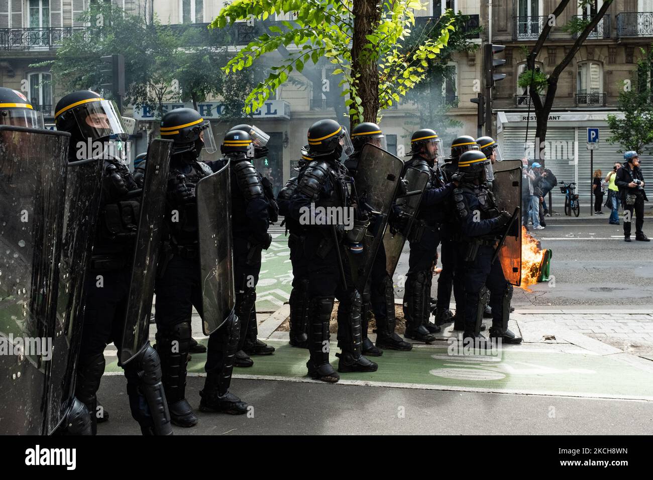 Anti-riot police officers standing near a burning trash can set on fire by demonstrators, while on July 14, 2021, 2 days after the last speech of the President of the French Republic Emmanuel Macron to introduce mandatory vaccination of caregivers and the generalization of the Sanitary Pass in public places of more than 50 people to cope with a resurgence of Covid in France following the emergence of the Delta variant, several hundred people gathered in the streets of Paris to demonstrate their opposition. This demonstration was quickly repressed by the riot police creating clashes with the de Stock Photo