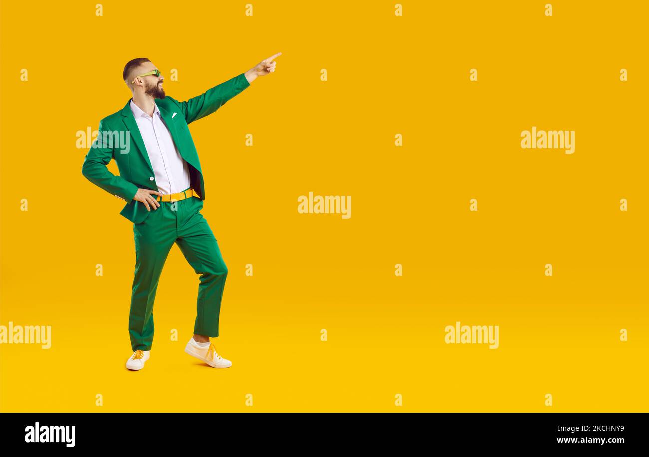 Confident handsome showman in green suit showing pointing on the right on yellow background. Stock Photo