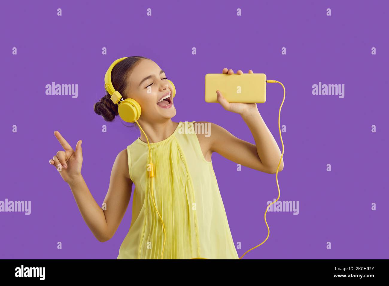 Cheerful preteen girl in headphones connected to mobile phone listens ...