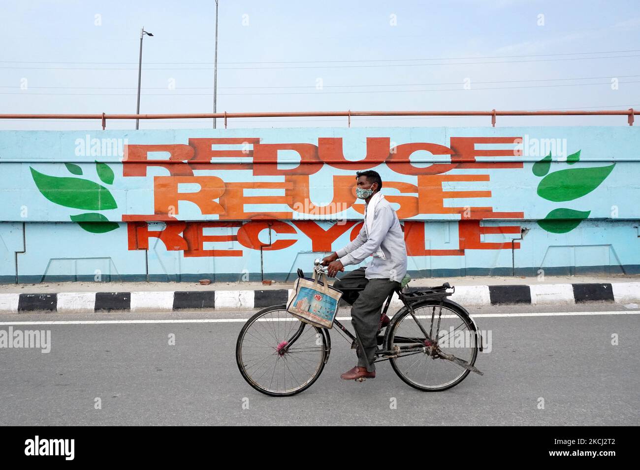 A man cycles past a graffiti reading 'Reduce, Reuse and Recycle' on a ...