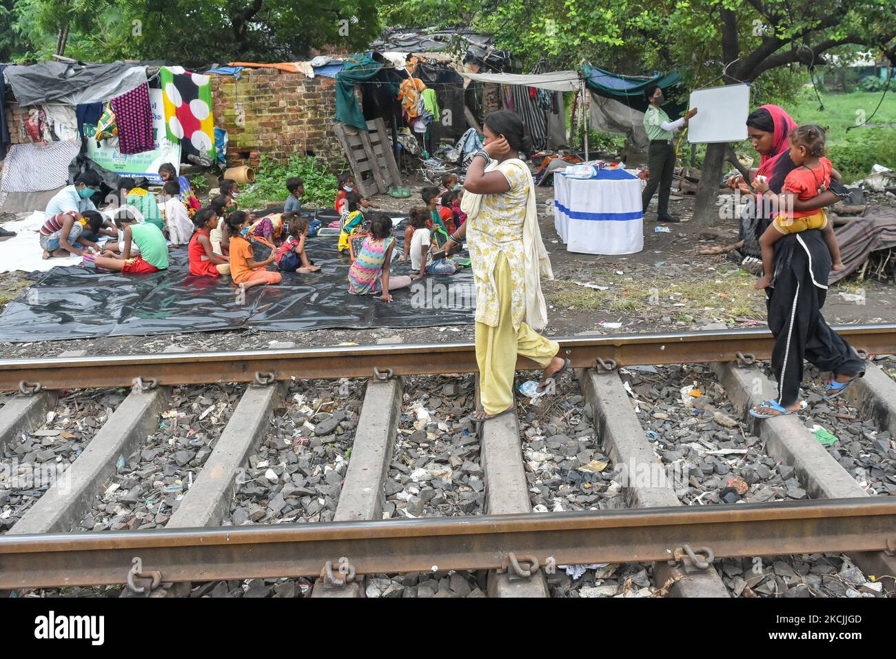 A lady volunteer of South West traffic guard teaching basic alphabets and numbering to chuildrens of a slum ,beside a railway track in Kolkata , India , on 13 August 2021 .A special class was organized by South west traffic guard to students belonging from slums of south Kolkata who cannot avail online classes or tuitions as all schools remain shut due to the pandemic. (Photo by Debarchan Chatterjee/NurPhoto) Stock Photo