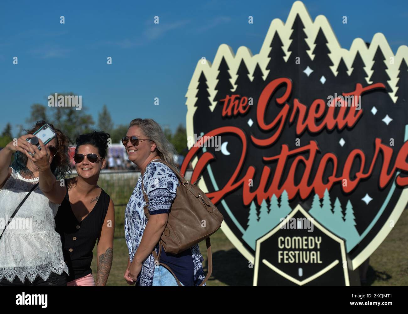Three ladies take a selfie next to a logo of the Great Outdoor Comedy