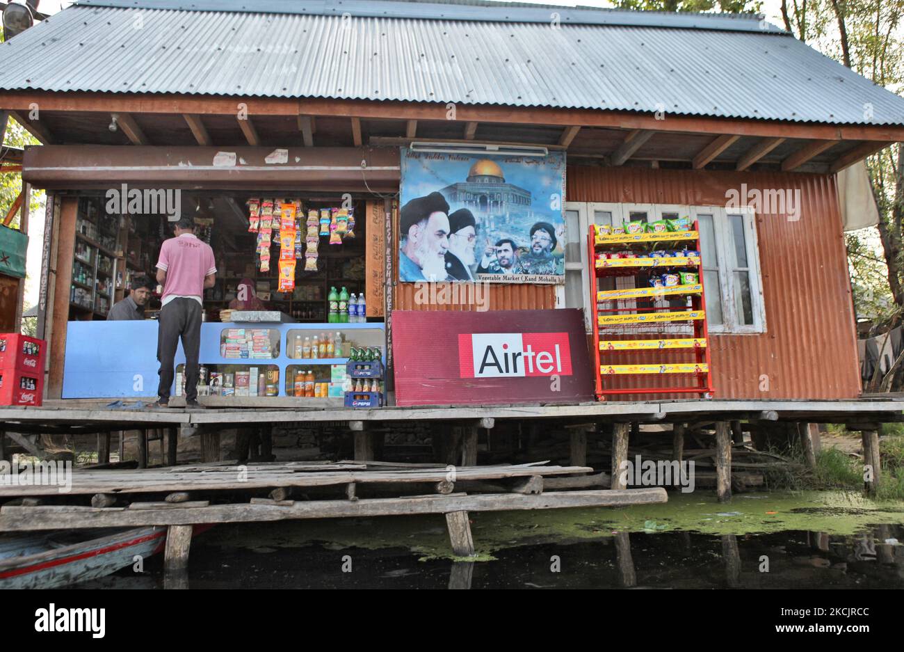 Kashmiri man buys goods from a floating shop with a large poster with ...