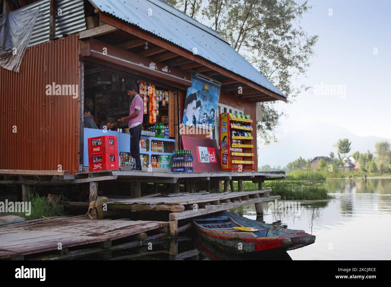 Kashmiri man buys goods from a floating shop with a large poster with ...
