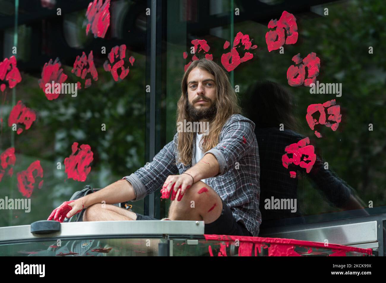 LONDON, UNITED KINGDOM - AUGUST 27, 2021: Environmental activists from Extinction Rebellion sit on top of the entrance to the Standard Chartered which has red paint spilled over the windows during a protest against the companies and institutions that are financing, insuring and enabling major fossil fuel projects and extraction of resources in the developing countries of the Global South, demanding change to the colonial system that drives the crises of climate and racism on 27 August 2021 in London, England. Extinction Rebellion activists target the City of London during the two week 'Impossi Stock Photo