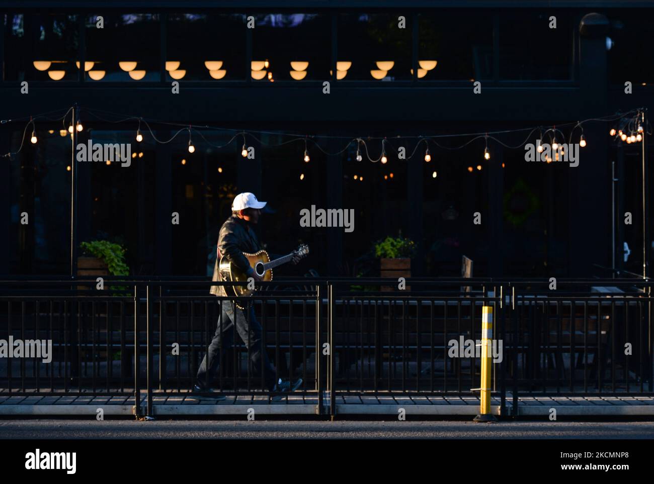 A Man Playing A Guitar Walks Past Empty Tables Outside A Restaurant On a-man-playing-a-guitar-walks-past-empty-tables-outside-a-restaurant-on