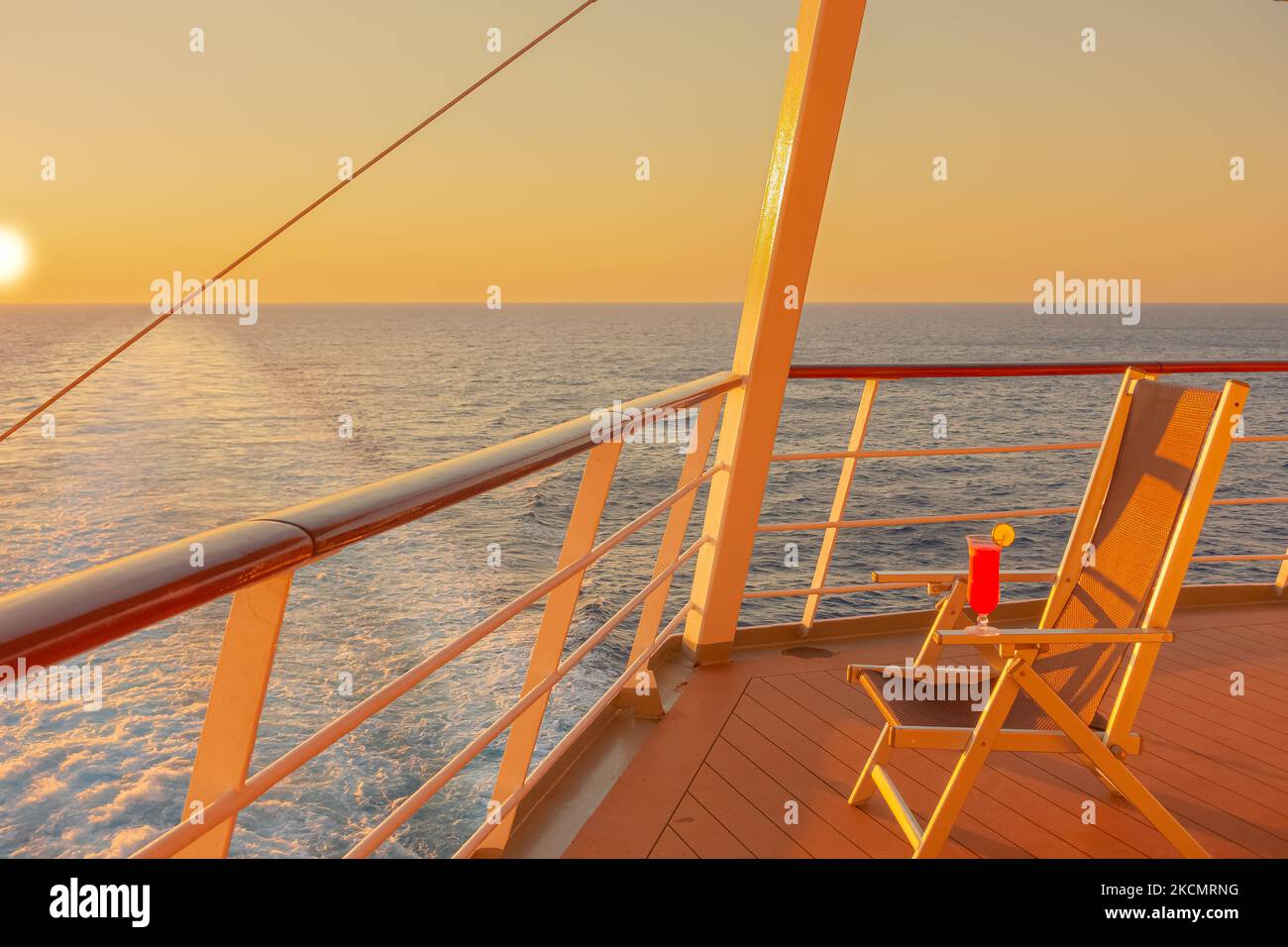 View of a strawberry daiquiri cocktail on the deck of a cruise ship at sunset in the wake of the cruise ship. View from the stern of the ship. Stock Photo