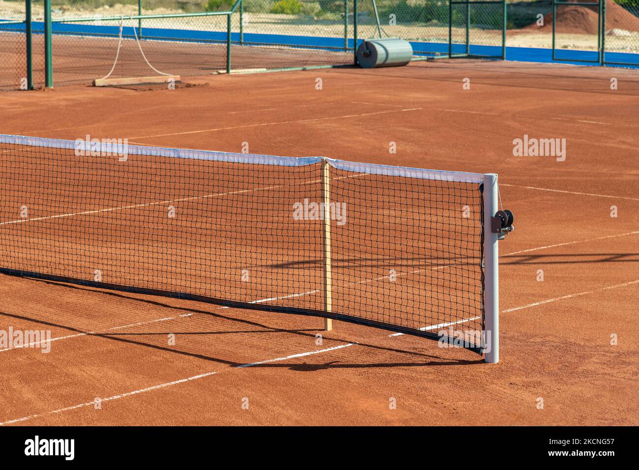 Baseline and net of an empty clay tennis court on a sunny day Stock Photo