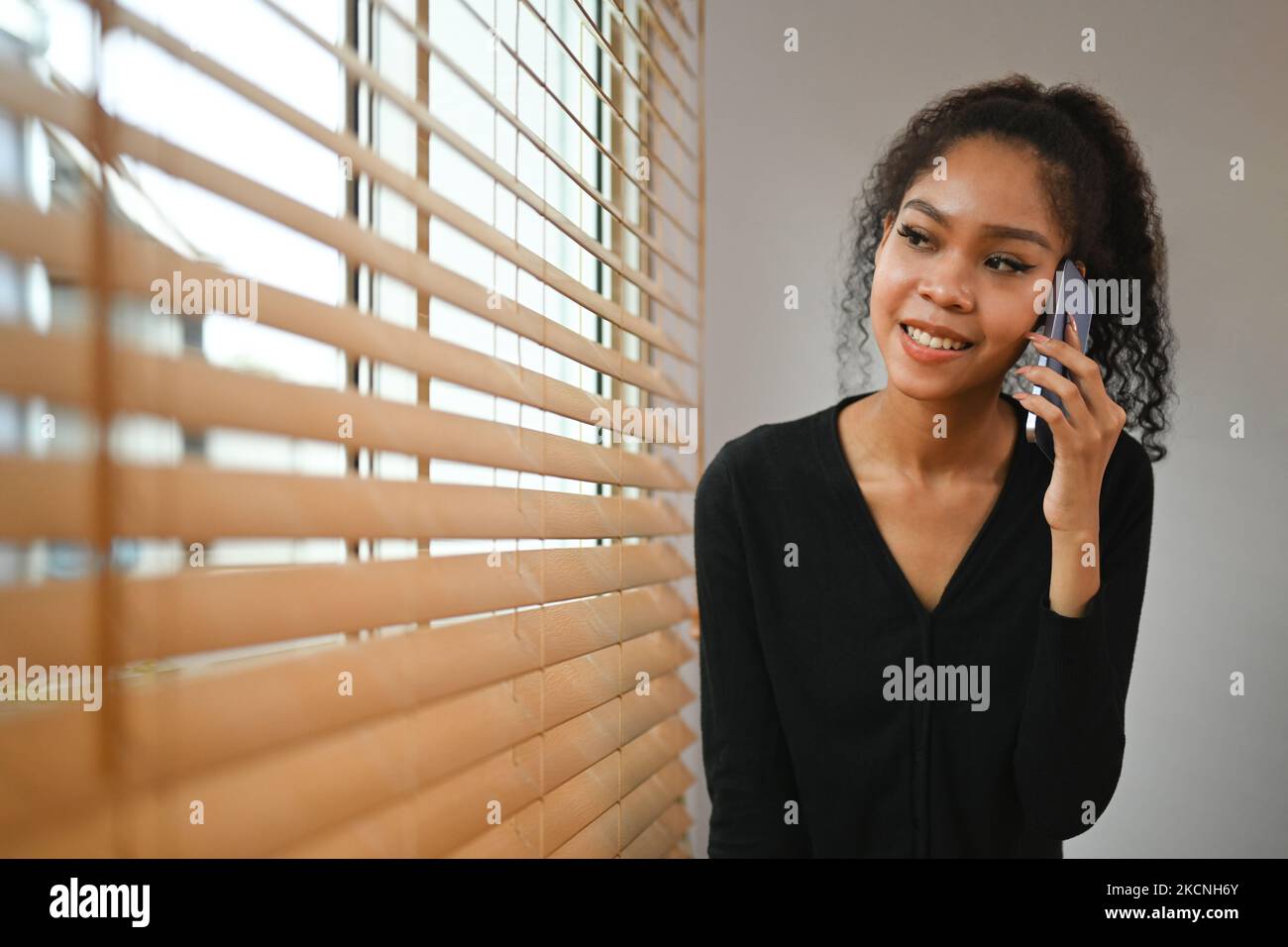 Smiling young African woman standing near window in home office and ...