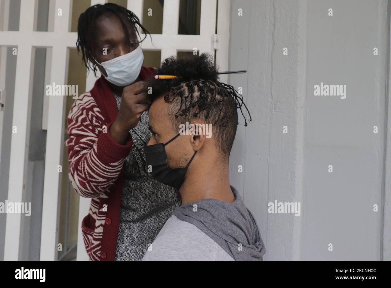 A Haitian migrant woman moulds a young man's hair inside the Casa de Acogida Formación y Empoderamiento de la Mujer Migrante y Refugiada (CAFEMIN), located in Mexico City, Mexico, on September 27, 2021, which offers accommodation and food to migrants who recently went to various refugee support offices to try to obtain a permit to stay longer in Mexico in view of the difficulties their compatriots are having in entering the United States during the COVID-19 health emergency. (Photo by Gerardo Vieyra/NurPhoto) Stock Photo