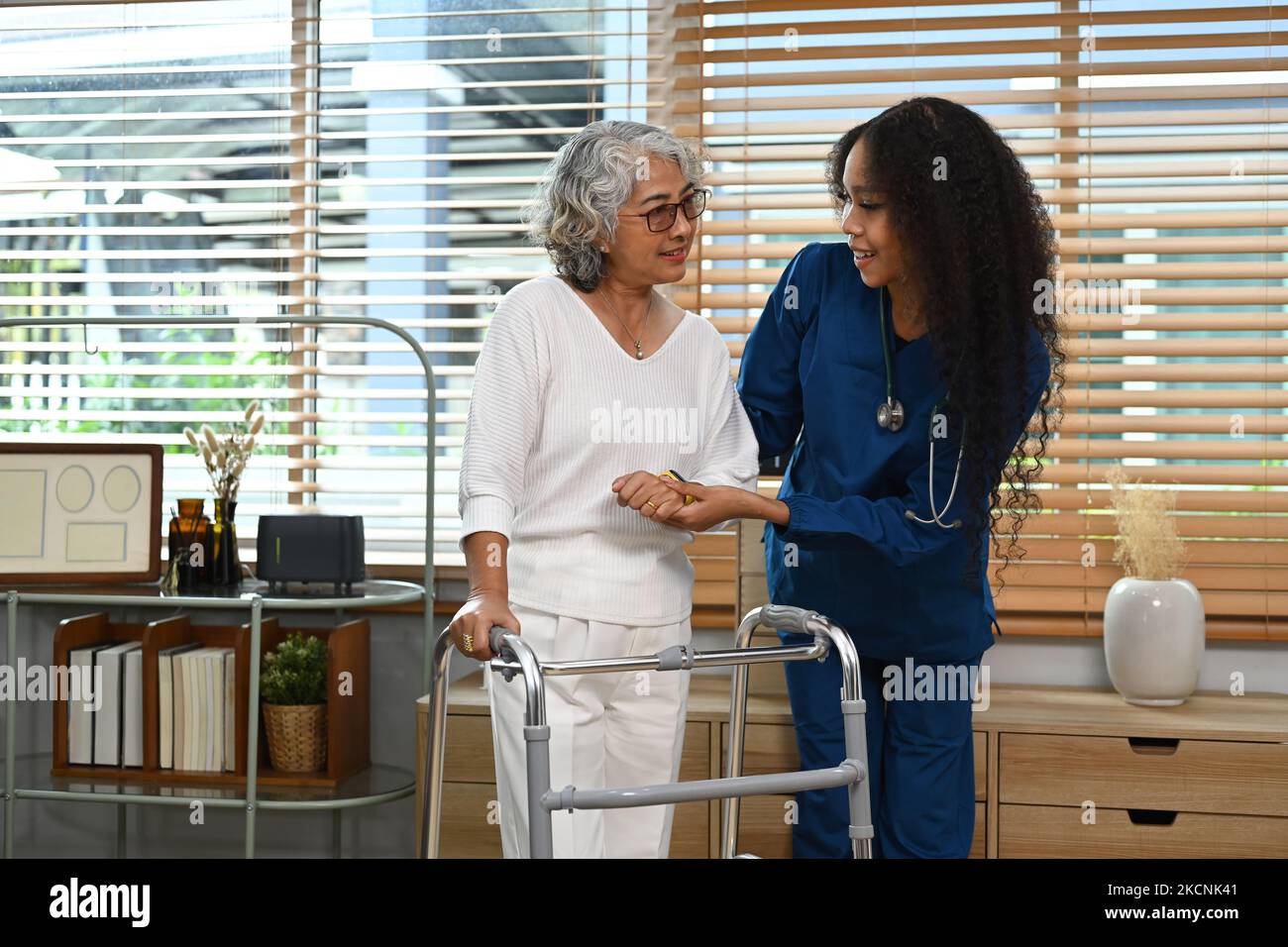 Shot of female caregiver is teaching senior woman to walk with walker. Assistance, rehabilitation and health Stock Photo