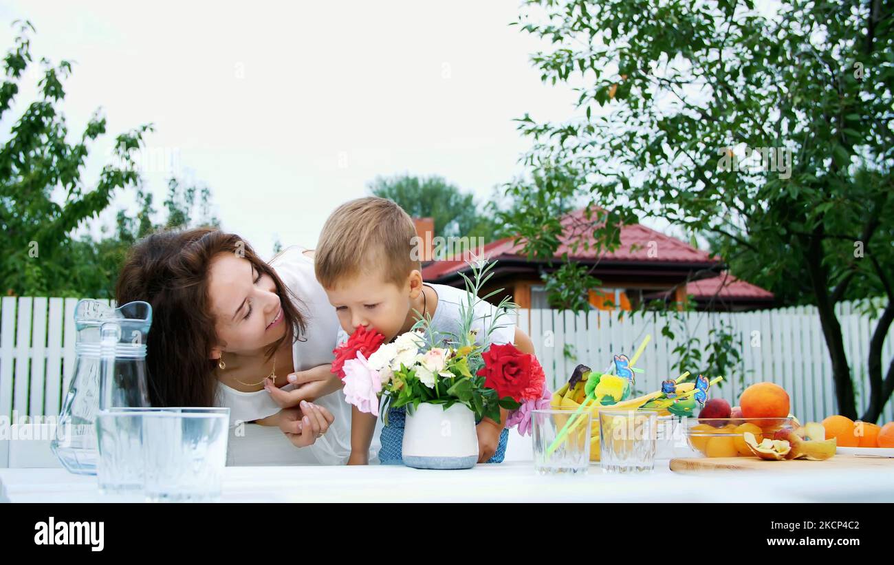 summer, in the garden. Mom with a four-year-old son make a bouquet of flowers. The boy likes it very much, having fun, sniffing flowers. The family spends their leisure time together. High quality photo Stock Photo