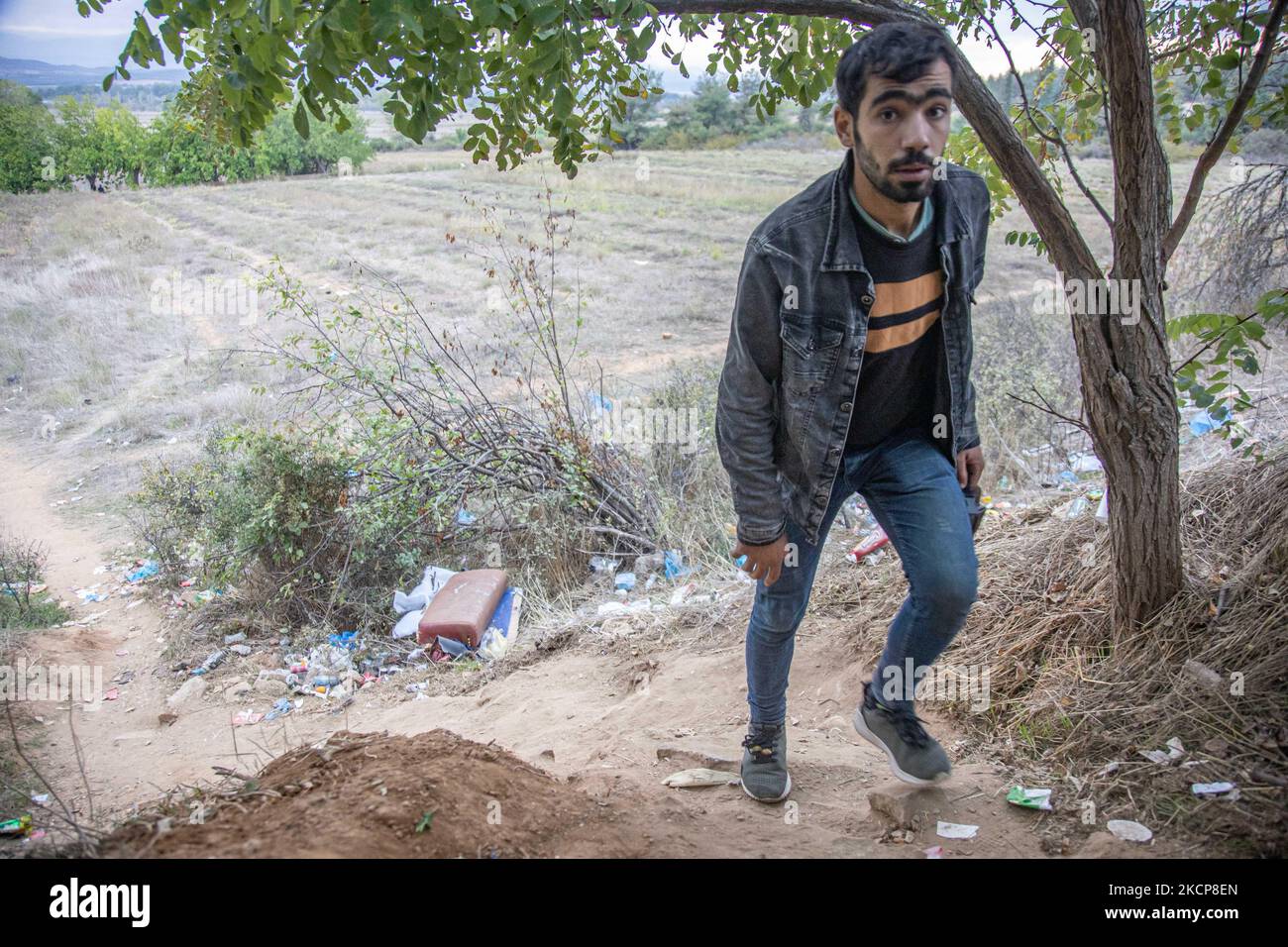Group of three young asylum seekers walking up to a hill as they return from their attempt to cross the borders. Asylum Seekers are trying to cross the Greek-North Macedonian borders to follow the Balkan Route, famous in 2015-2016 during the Syrian refugee crisis, from Idomeni, Greece to Gevgelija, North Macedonia following the train rails and railway station and then reach central and northern Europe. Refugees and Migrants are seen walking in the fields in the Greek side, before the fence that separates the two countries, trying to reach and pass the borders. The small groups are mostly male  Stock Photo
