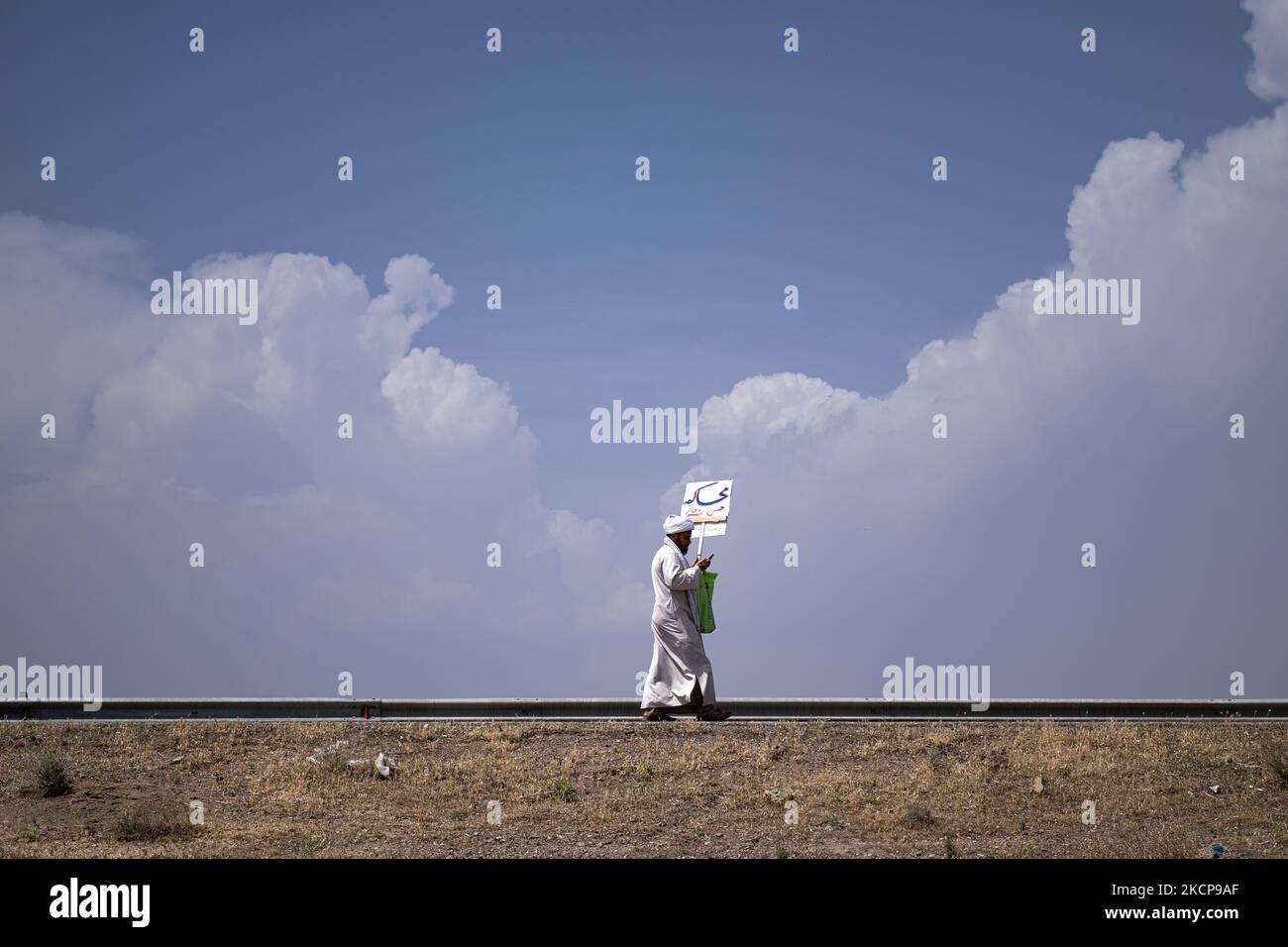 An Iranian cleric carrying a placard with a Persian script that reads, Trial for Hassan Rouhani (Former Iranian president), while walking along a road from the holy city of Qom to Tehran on April 14, 2021. (Photo by Morteza Nikoubazl/NurPhoto) Stock Photo