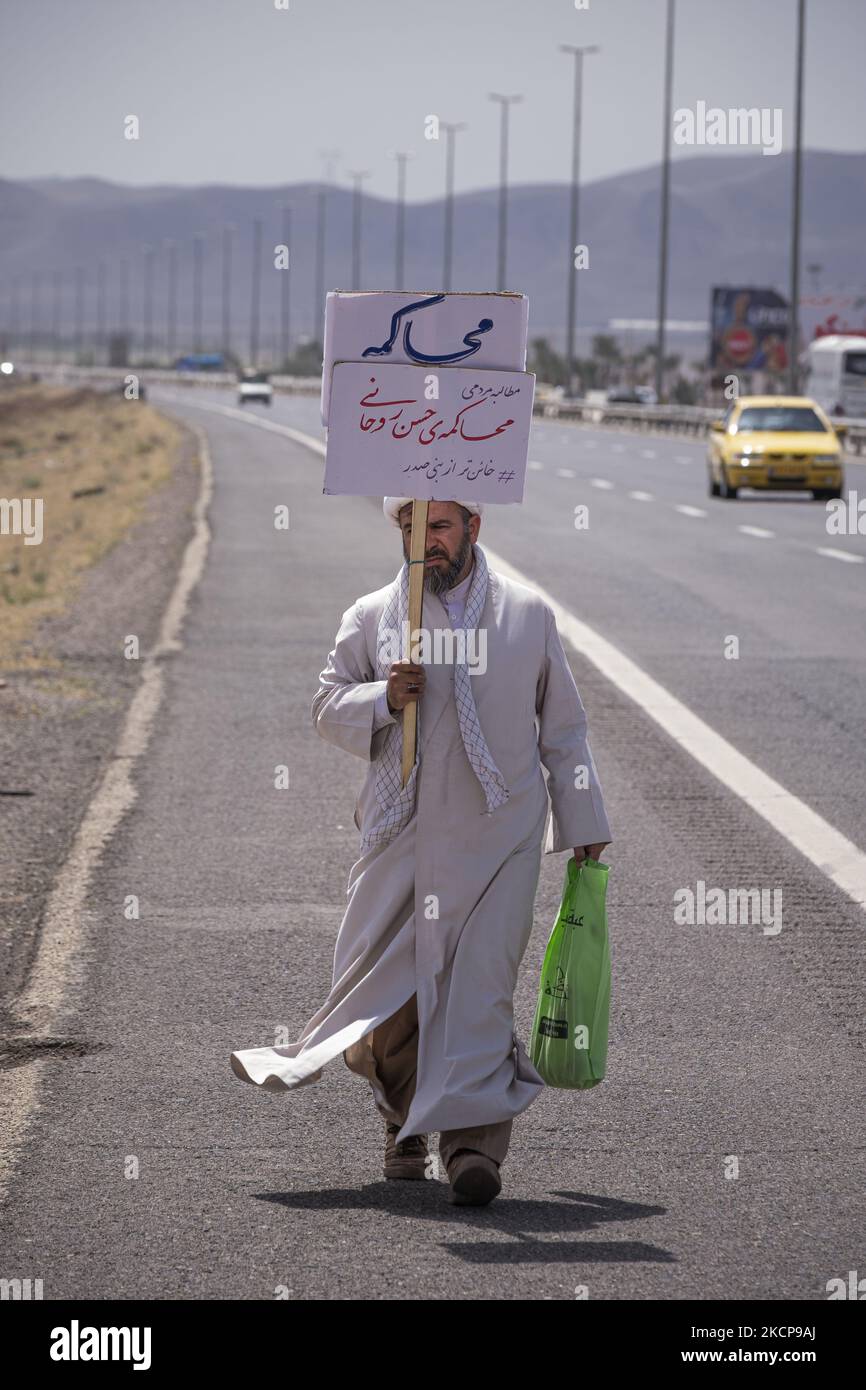 An Iranian cleric carrying a placard with a Persian script that reads, Trial for Hassan Rouhani (Former Iranian president), while walking along a road from the holy city of Qom to Tehran on April 14, 2021. (Photo by Morteza Nikoubazl/NurPhoto) Stock Photo