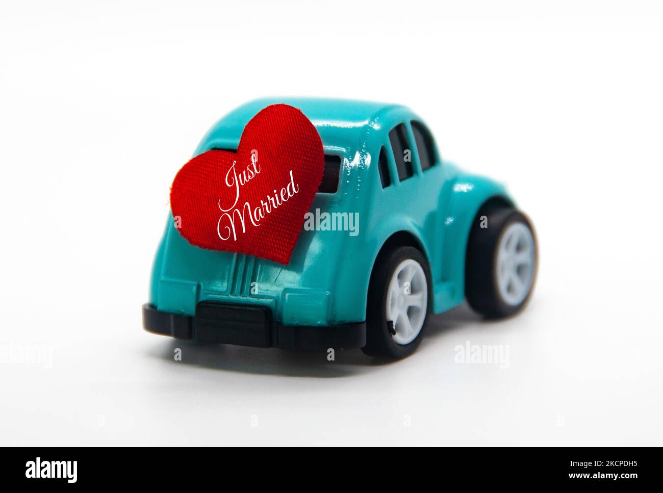 Mini toy car carrying red heart shape with text Just Married. Newly wed
