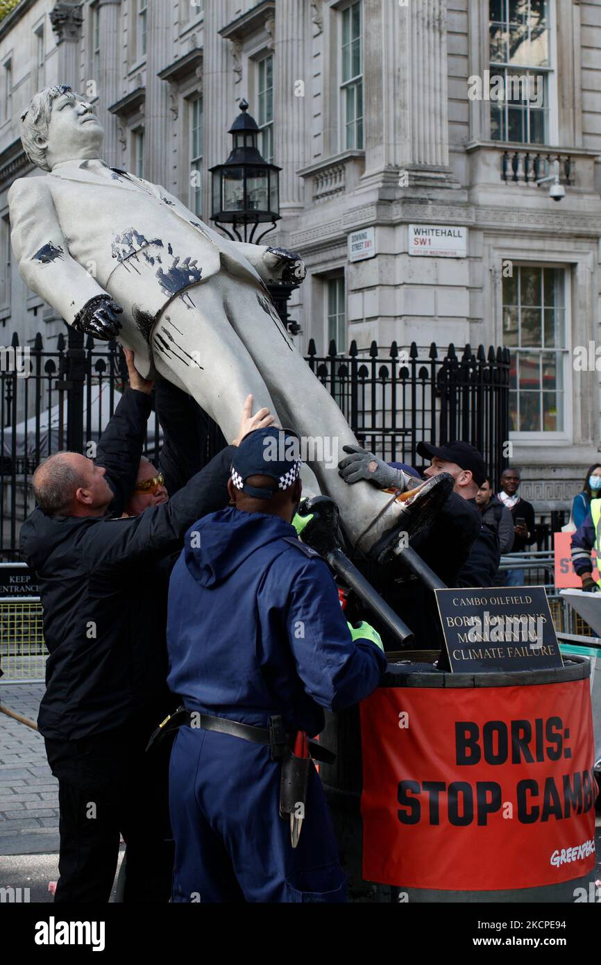 Police officers take down an oil-smeared mock statue of British Prime Minister Boris Johnson after removing Greenpeace activists 'locked-on' to oil drums outside the gates of Downing Street on Whitehall in London, England, on October 11, 2021. The protest was staged to protest permission sought by energy company Siccar Point from British authorities for drilling at the Cambo oilfield in the North Sea. (Photo by David Cliff/NurPhoto) Stock Photo