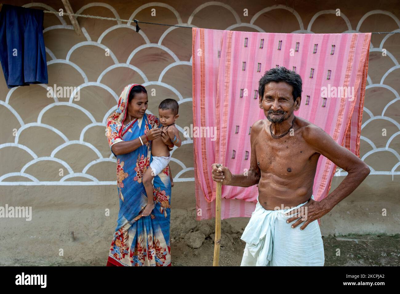 A man poses with his family in front of a painted wall in alpona village in chapainawabganj, Bangladesh (Photo by Mushfiqul Alam/NurPhoto) Stock Photo