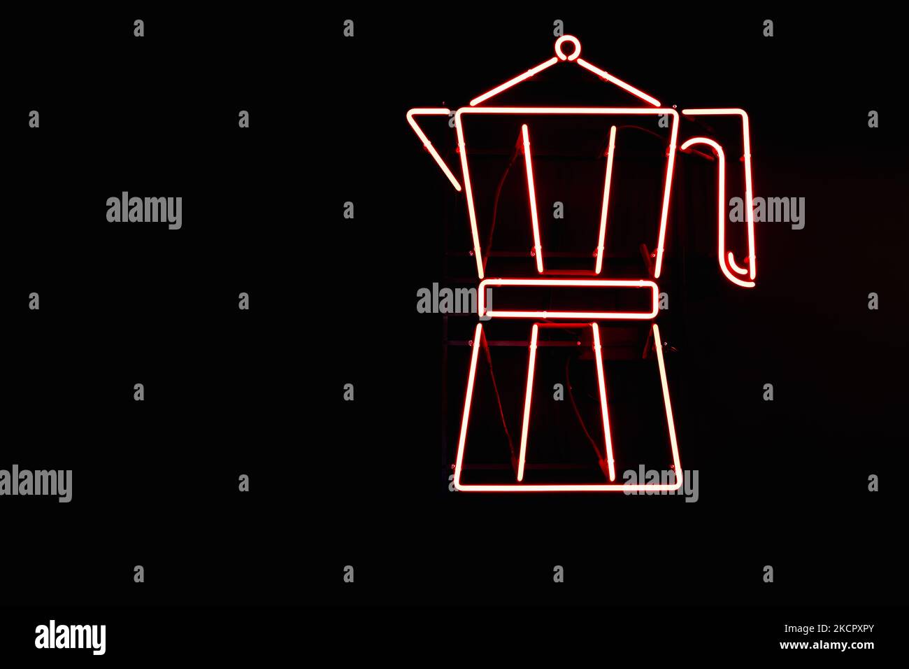 Red neon sign from lamps in the form of a Moka pot coffee maker on the wall of a black coffee shop. Stock Photo
