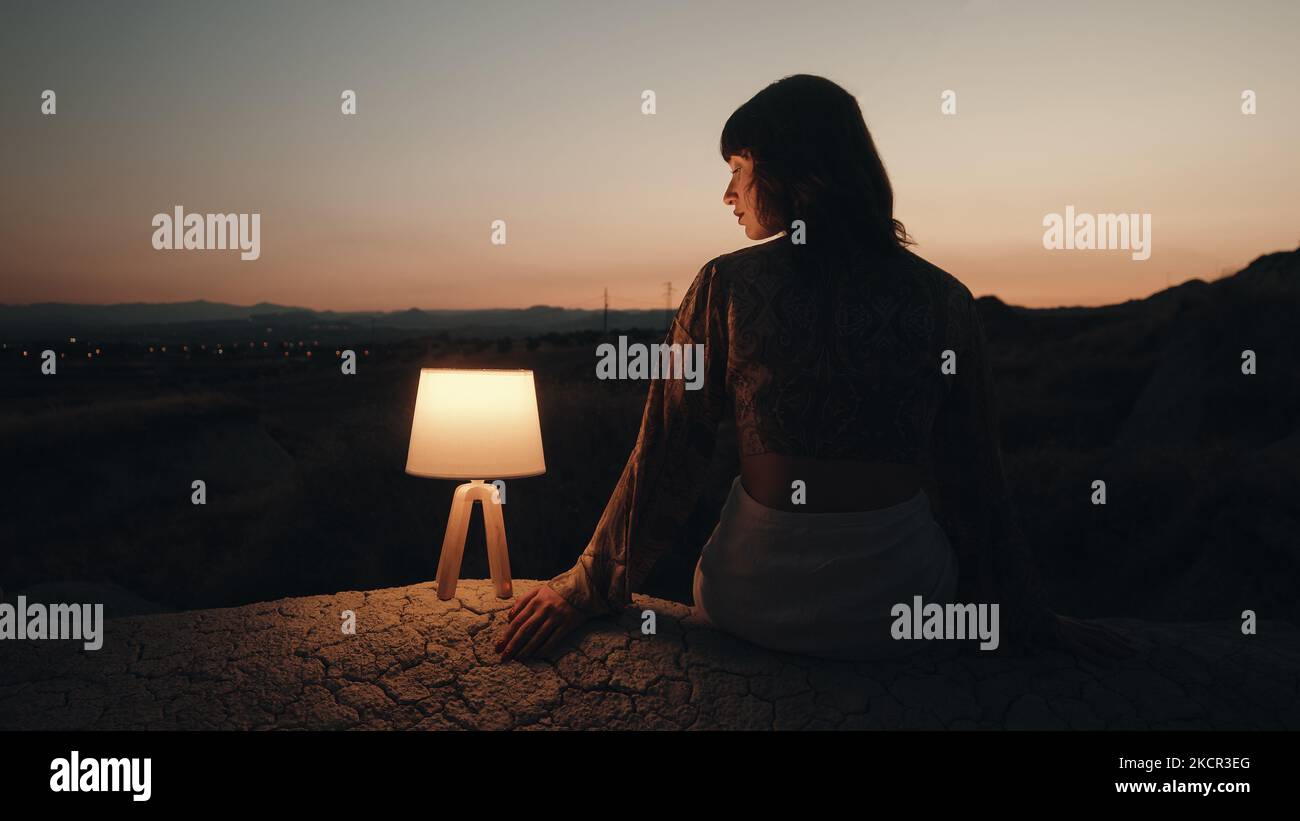 Silhouette of a girl sitting on the rock with lamp at sunset Stock ...