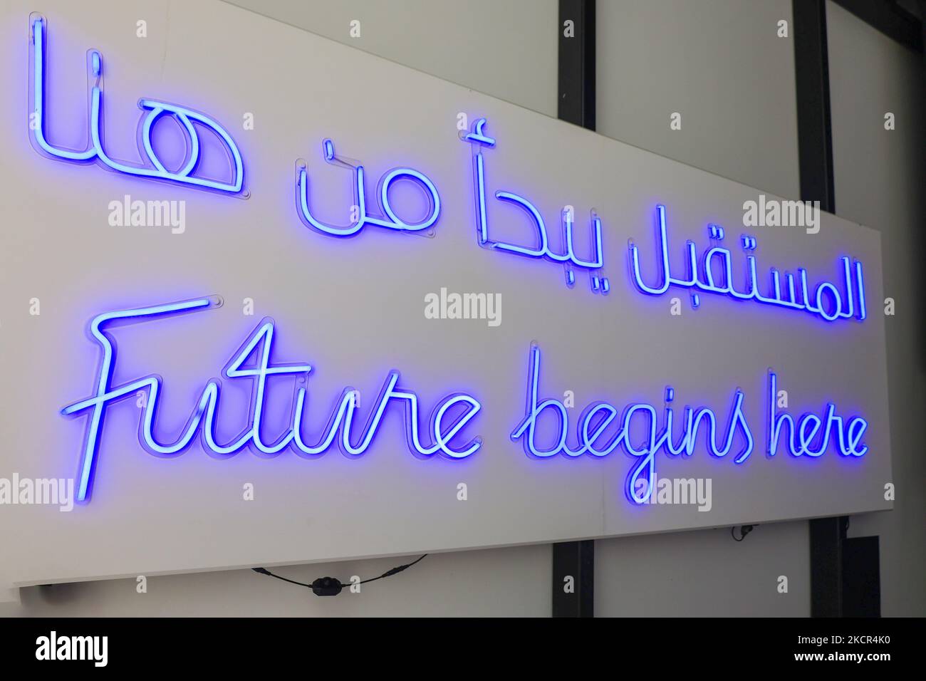 Blue neon signs FUTURE BEGINS HERE in English and Arabic on wall . High quality photo Stock Photo