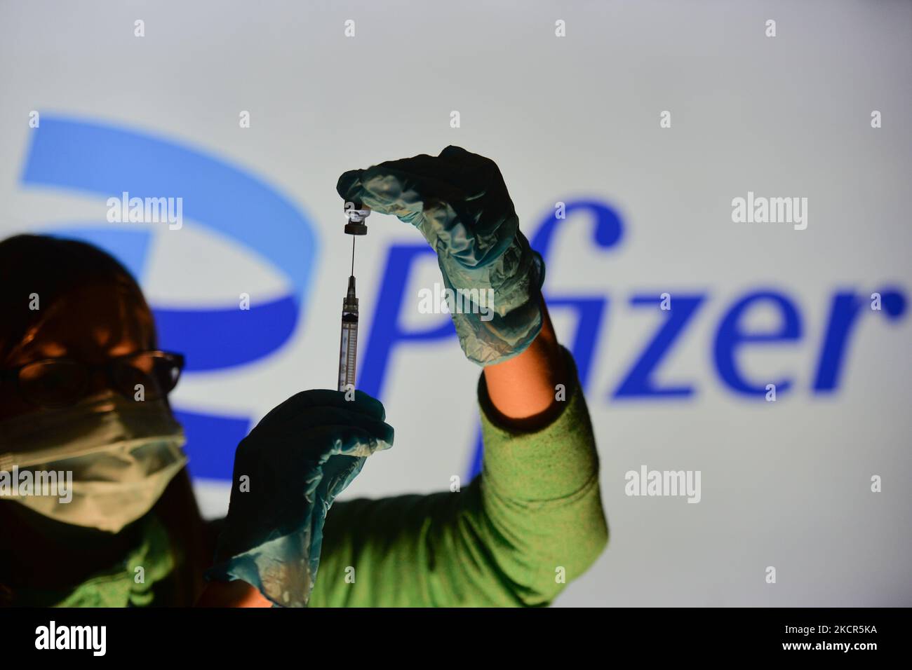 An illustrative image of a person holding a medical syringe and a vaccine vial in front of the Pfizer logo displayed on a screen. On Thursday, October 21, 2021, in Edmonton, Alberta, Canada. (Photo by Artur Widak/NurPhoto) Stock Photo