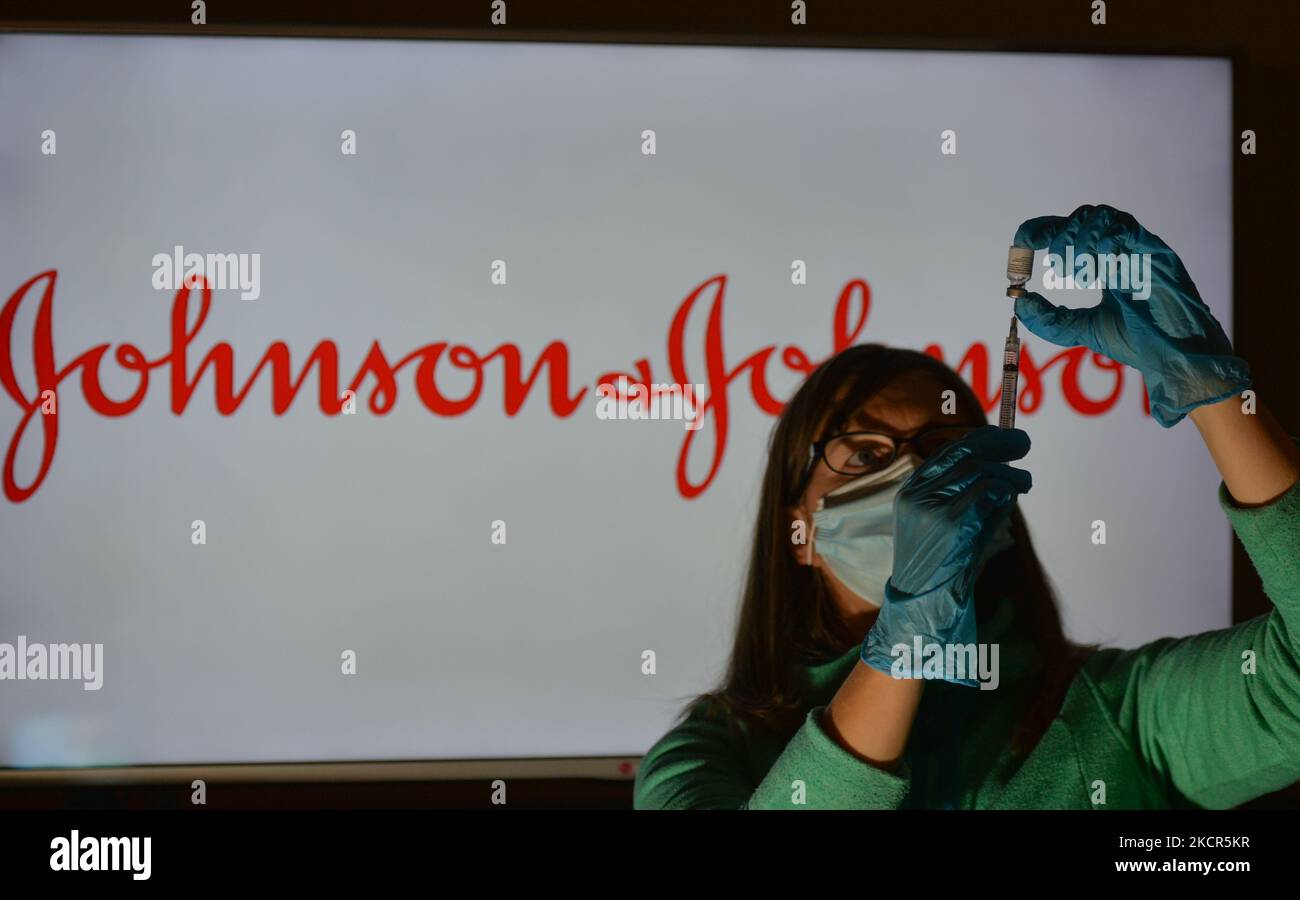An illustrative image of a person holding a medical syringe and a vaccine vial in front of the Johnson and Johnson logo displayed on a screen. On Thursday, October 21, 2021, in Edmonton, Alberta, Canada. (Photo by Artur Widak/NurPhoto) Stock Photo